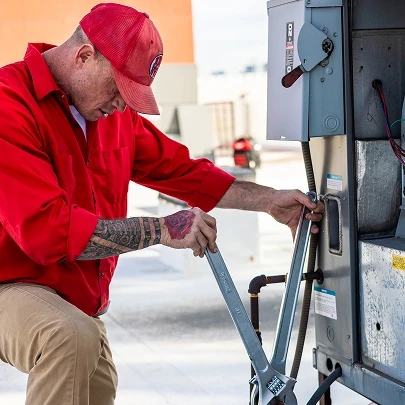 HVAC service technician in a red uniform knocking on a residential front door.