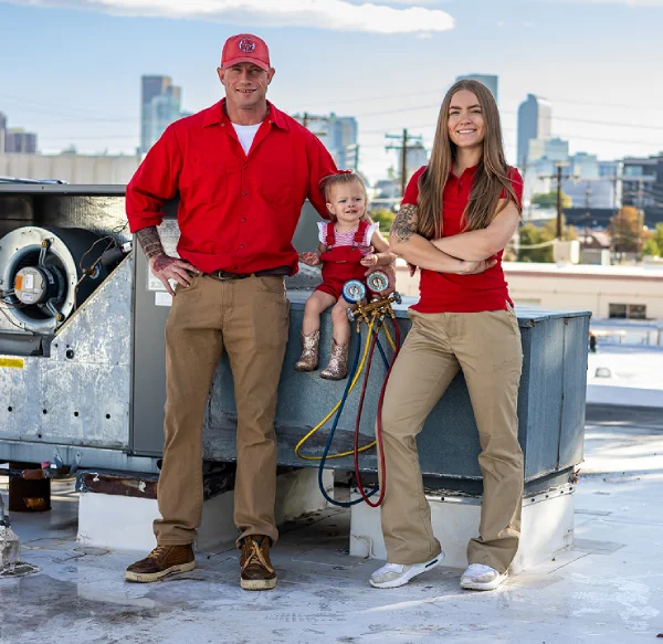 A family posing next to a commercial HVAC unit on a rooftop with a city skyline background.