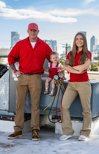 Vertical portrait of the JUMP HVAC family service team posing together next to a rooftop AC unit with the Denver city skyline behind them.