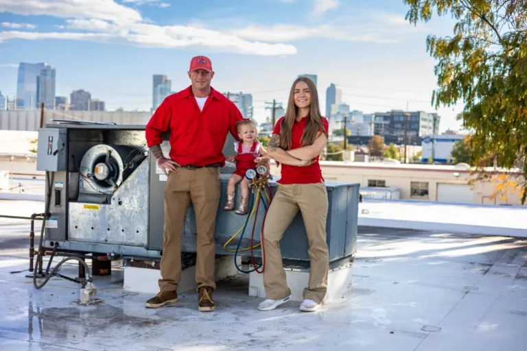 Two HVAC technicians and a small toddler standing beside a rooftop air conditioning system with a city skyline view.