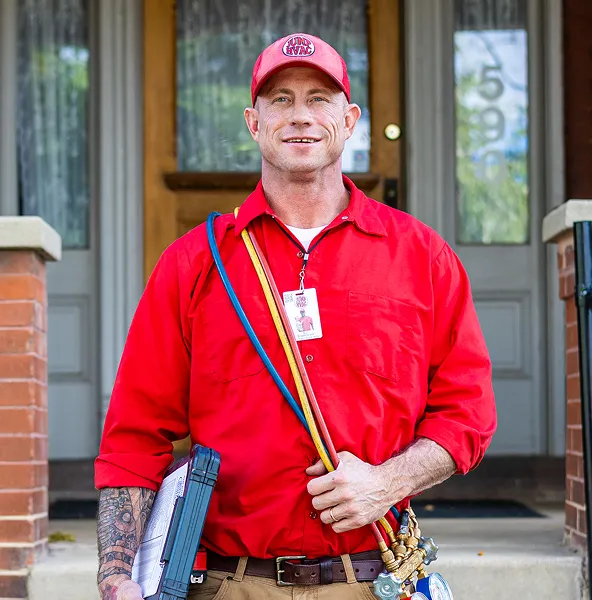 Professional HVAC technician in a red uniform carrying pressure manifold gauges on his shoulder.