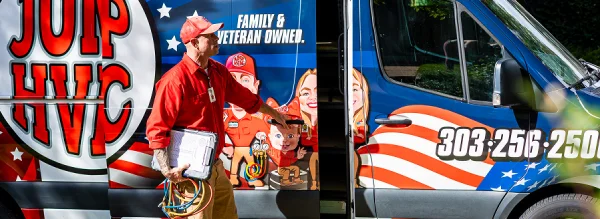 HVAC technician in a red uniform carrying a white binder next to a heavily wrapped service vehicle.