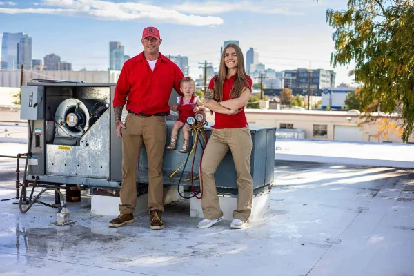HVAC repair technicians and a young child posing next to a commercial rooftop ventilation unit.