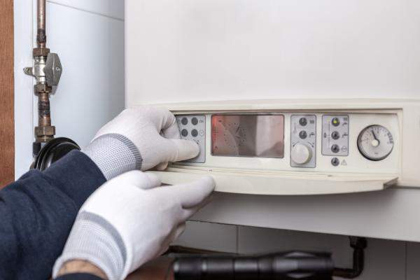 Hands in gloves adjusting settings on a wall-mounted boiler control panel.