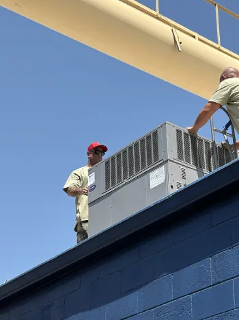 HVAC service technician with arm tattoos inspecting a commercial Trane rooftop package unit.