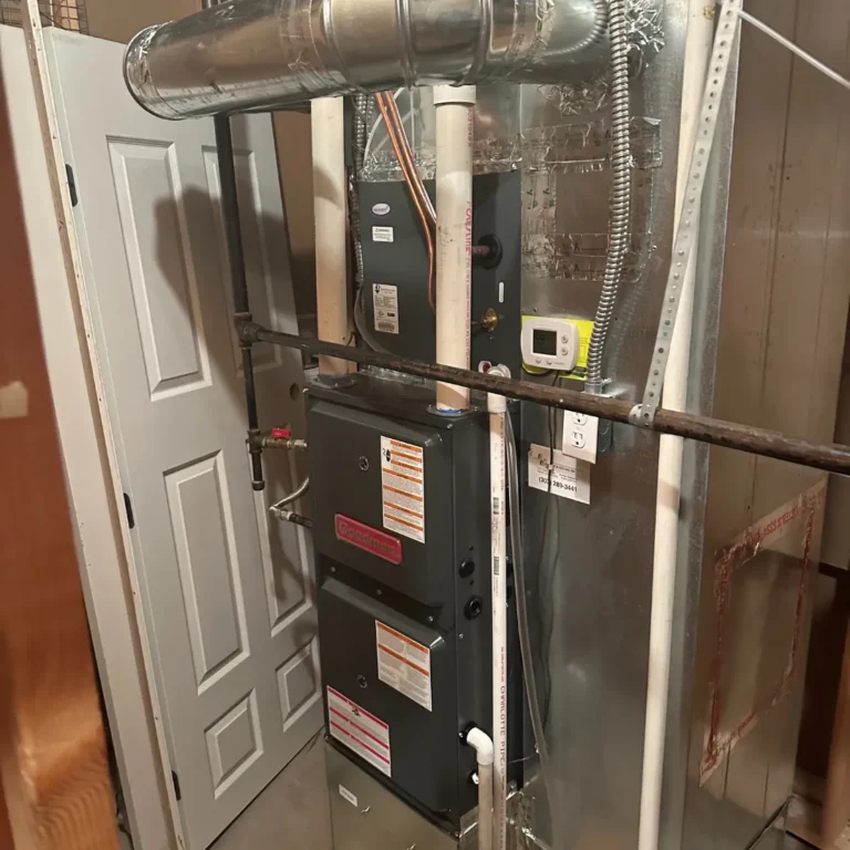 Residential gas furnace unit with metal ductwork and PVC pipes inside a utility closet.