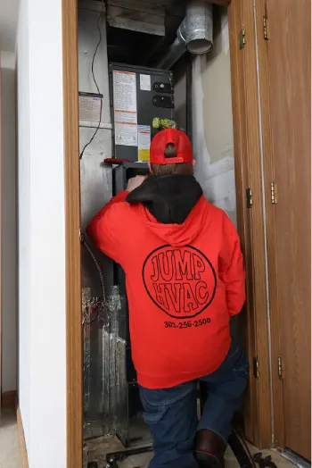 HVAC service technician in a red uniform knocking on a residential front door.